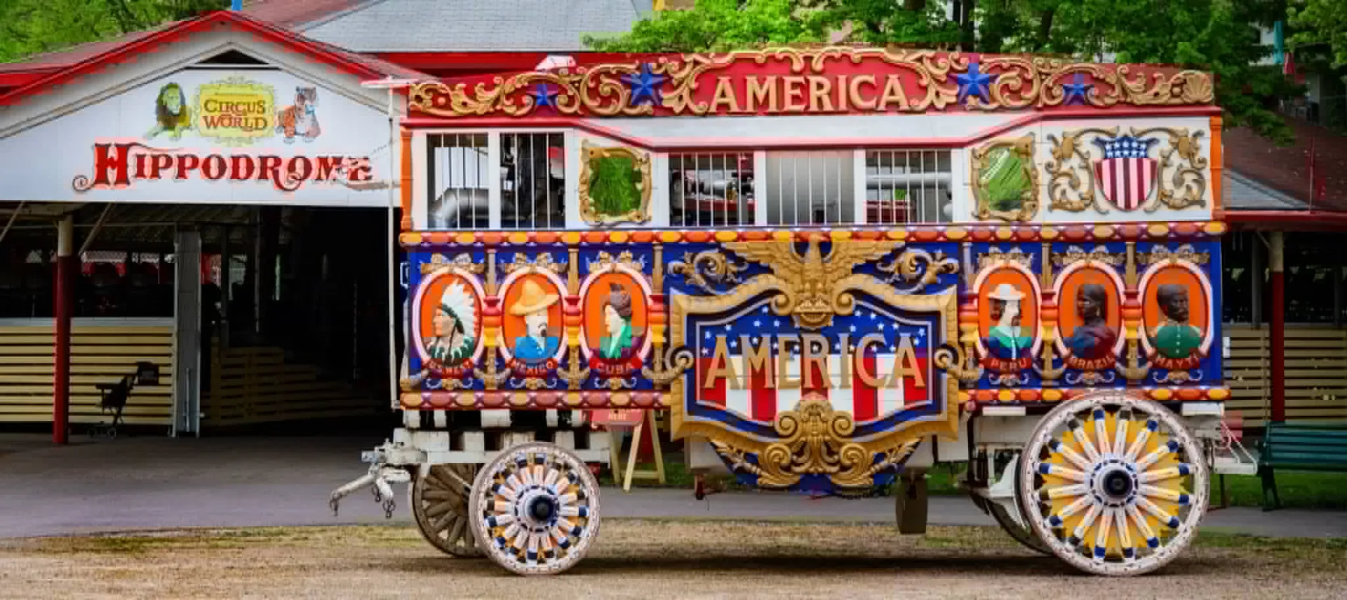 Colorful vintage circus parade wagon displayed outside the Hippodrome building at Circus World, featuring ornate patriotic artwork and decorative wheels.