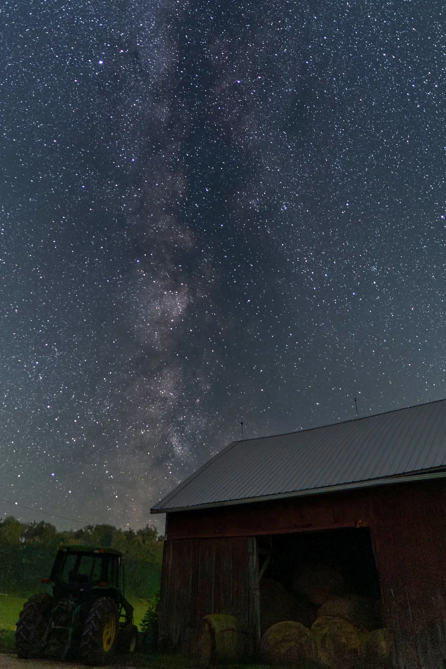 Milky Way stretching across the night sky above a red barn and tractor at Valley Springs Farm Bed & Breakfast, showcasing excellent stargazing in the Wisconsin countryside.