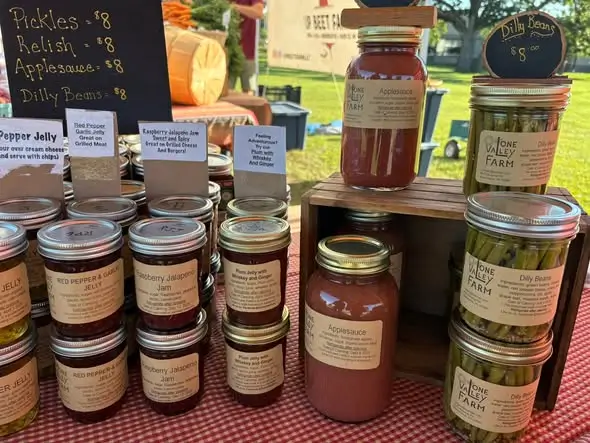 Locally made jams, pickles, applesauce, and other farm products at a farmers market stand.